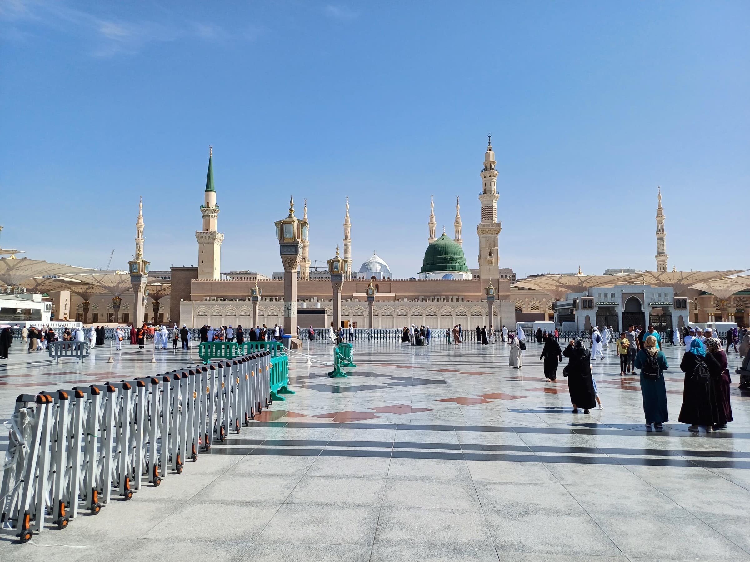 The open courtyard of Masjid an-Nabawi with its large shade umbrellas and minarets on a clear day